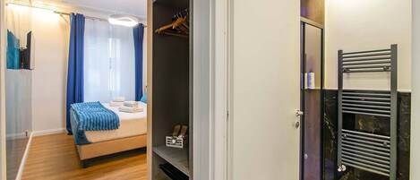 A bedroom with a bed, a wardrobe, and a bathroom with a towel rack.