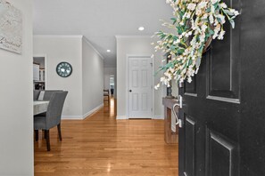 A hallway with a dining area, a clock, and a door with a floral arrangement.