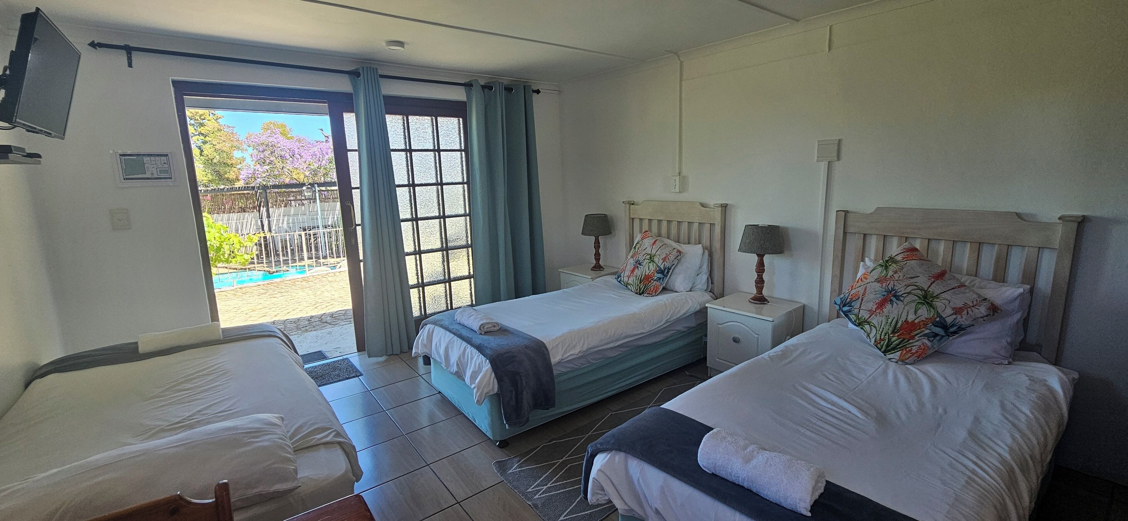 A hotel room with two beds, a small table, a chair, a TV, and a sliding glass door leading to a pool area.
