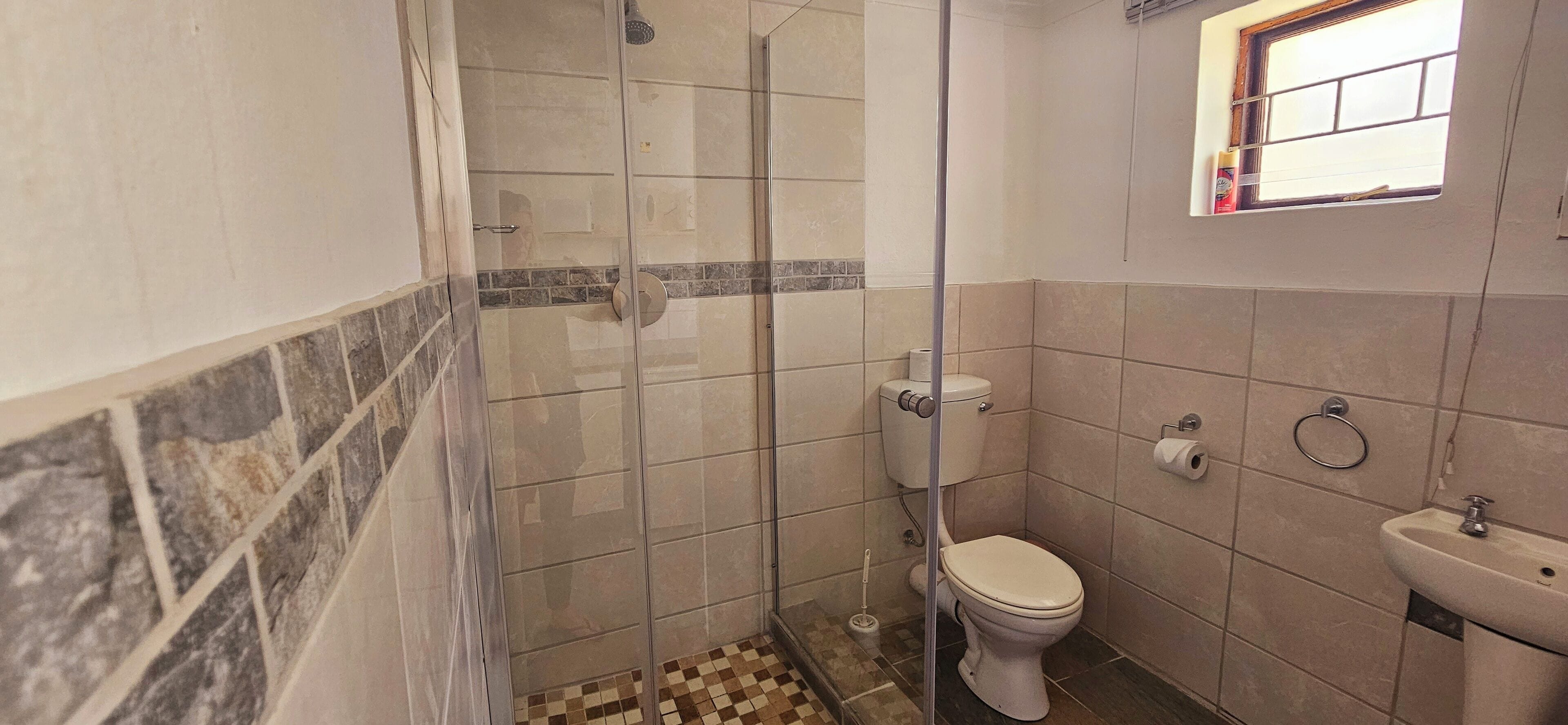 A bathroom with a glass-enclosed shower, a toilet, a sink, and a small window.
