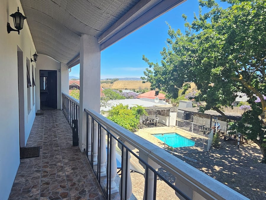 A covered balcony with a stone floor, a pool, and a view of a rural landscape.