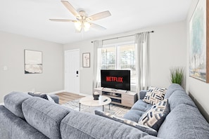 A modern living room with a grey sofa set, a coffee table, a TV on a wooden stand, and a ceiling fan.