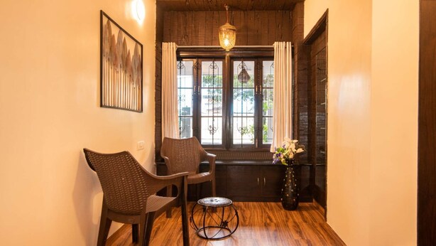 Una habitación acogedora con suelo de madera, una silla de mimbre, una pequeña mesa redonda y una lámpara colgante.