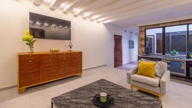 Uma sala de estar moderna com uma televisão de tela plana grande, um armário de madeira, um sofá com almofada amarela e uma mesa de centro de mármore.