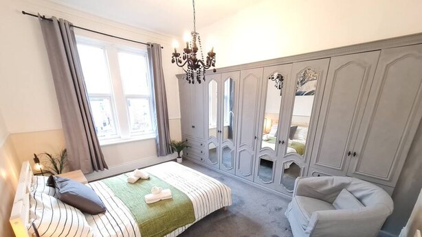 Ein Schlafzimmer mit Bett, Nachttisch, Lampe, Kleiderschrank und einem Sessel.