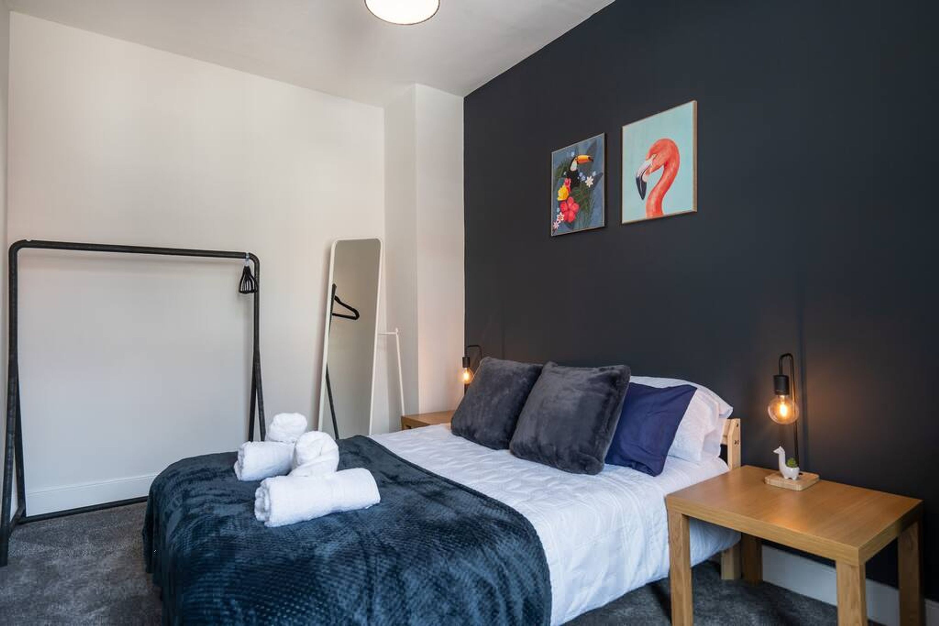 Een moderne hotelkamer met een bed, een houten nachtkastje, een wandlamp en twee kunstwerken.