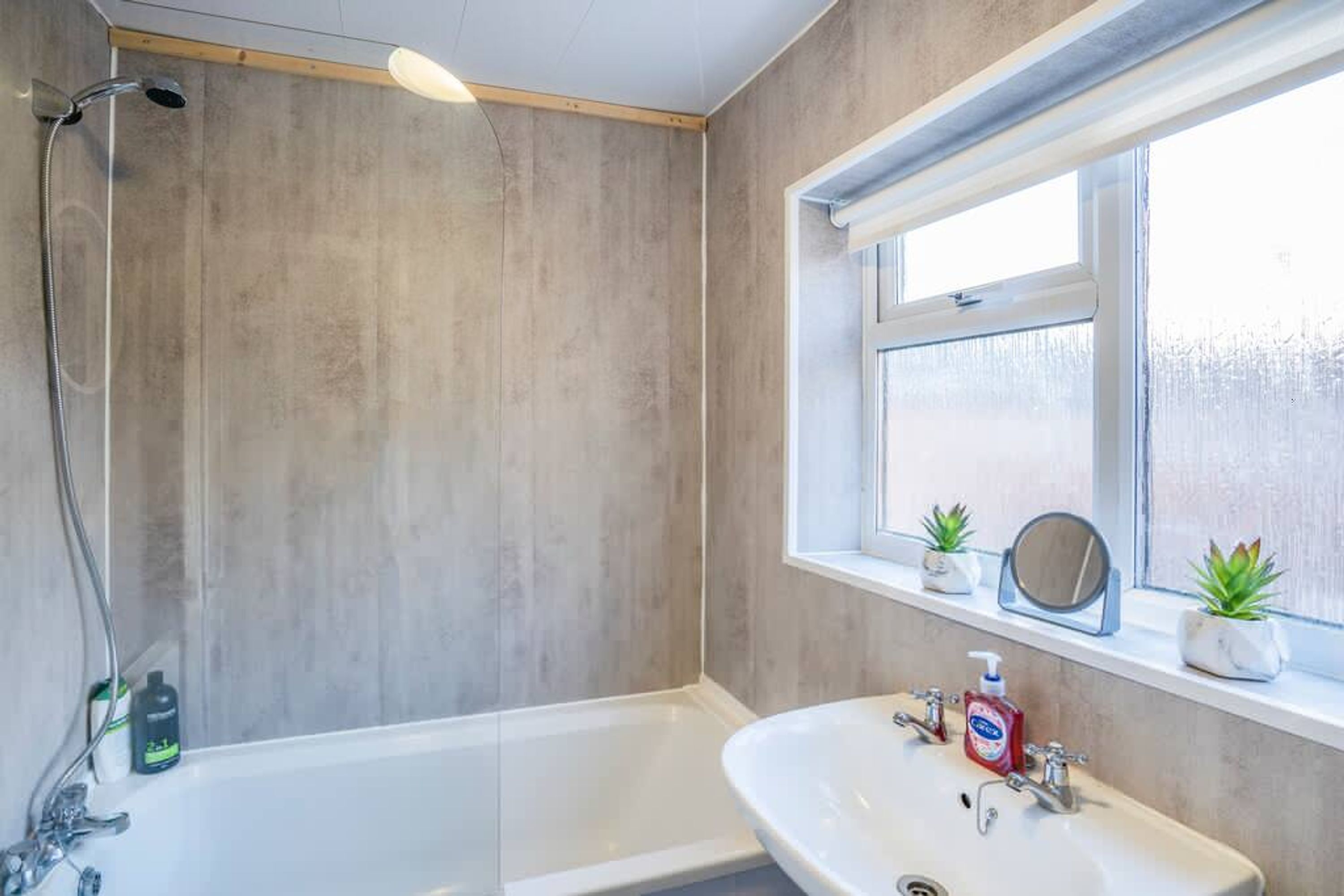 A bathroom with a bathtub, a sink, and a window with plants.
