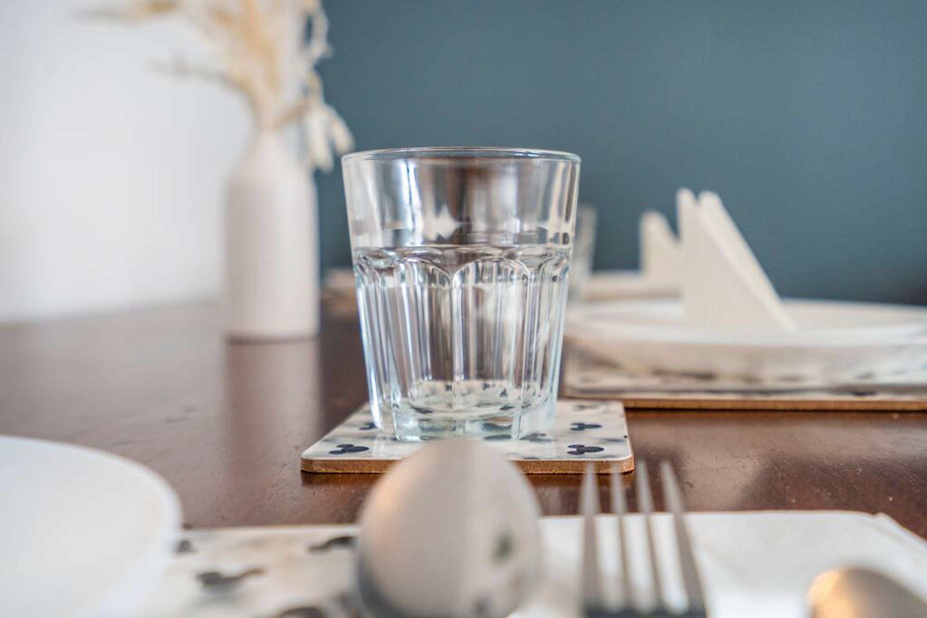 A clear glass of water on a coaster, a spoon, and a fork on a table with a placemat.