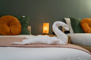 Una toalla con forma de cisne sobre una cama con una manta rosa, dos almohadas y una mesita de noche iluminada en una habitación de hotel.