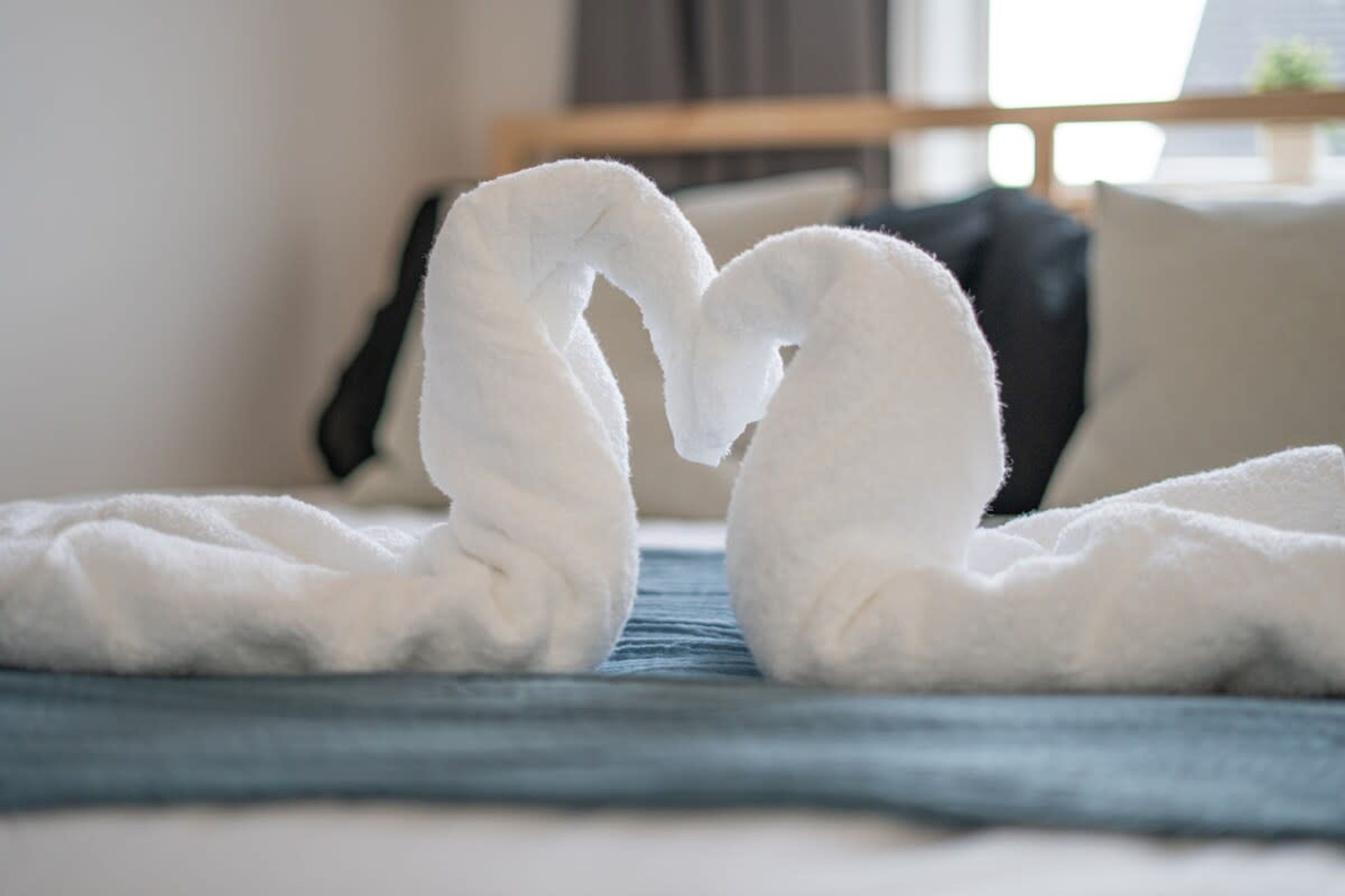 A bed with a blue blanket and two white towels arranged in a heart shape.