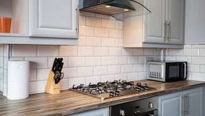 A kitchen with white cabinets, a gas stove, a microwave, and a wooden countertop. - Large 3 Bed Apartment-sea Road (Sunderland)