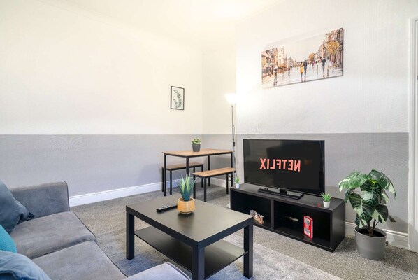A living room with a sofa, a coffee table, a TV on a stand, a small table with chairs, and a potted plant. - 3 Bed-free Parking-close to City (Gateshead)
