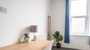 A room with a wooden desk, a lamp, a potted plant, a mirror, and a window with blue curtains. - 3 Bed-free Parking-close to City (Gateshead)