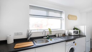 A modern kitchen with a built-in washing machine, a sink, and a window with blinds. - Modern - 2 Bed - Free Parking (Durham)