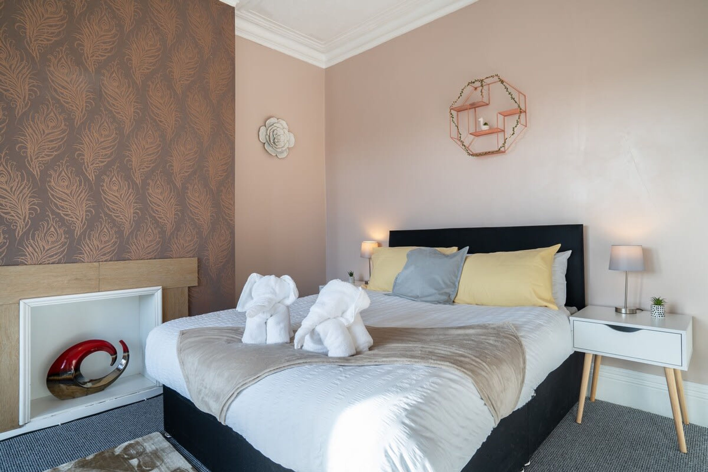 A neatly made bed with white linens, a black headboard, and a bedside table with a lamp.