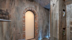 A bathroom with a stone wall, a brick archway, a white bathtub, and a shower area. - Stylish 2 Bed Flat-free Parking (Gorebridge)
