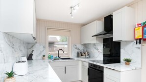 Una cocina moderna con armarios blancos, estufa negra y encimera de mármol.
