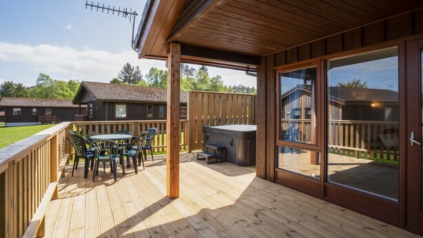 Una terraza de madera con mobiliario exterior, un jacuzzi y vistas a casas vecinas.