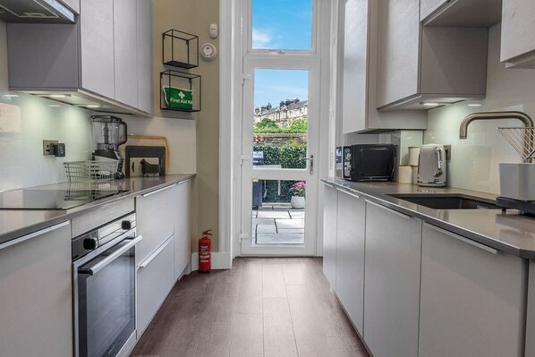 A modern kitchen with white cabinets, a built-in oven, a microwave, and a coffee machine. - Stylish Elegance in City s Heart (Edinburgh)