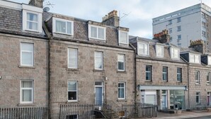 A row of terraced houses with stone facades, a gated entrance, and a visible shop with a sign. - 1 Bedroom Apartment-free Parking (Aberdeen)