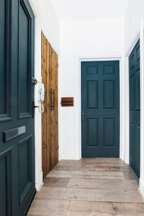 Een gang met een houten deur, een donkerblauwe deur en een witte muur met een brievenbus.
