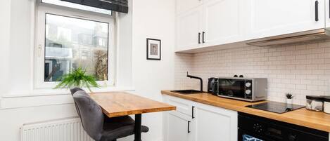 A modern kitchen with white cabinets, a wooden countertop, a black stove, and a window with blinds.