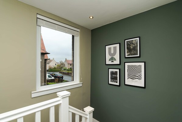 A staircase with a white railing, a window with a view of a street, and three framed artworks on the wall. - 3 Bedroom House-free Parking (Broxburn)