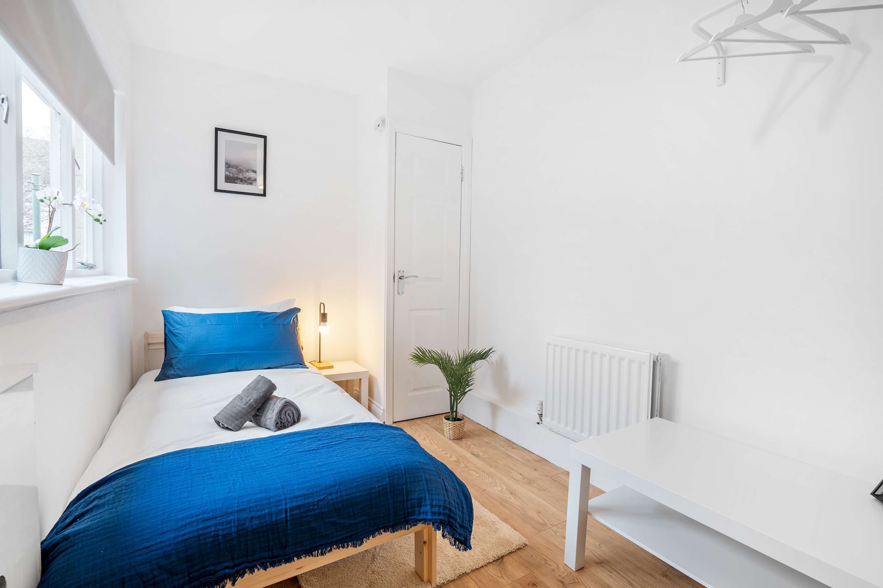 A bedroom with a bed, a bedside table, a lamp, a radiator, and a door.