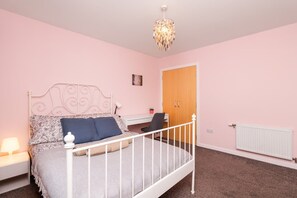 A bedroom with a bed, bedside table, lamp, desk, chair, wardrobe, and radiator.