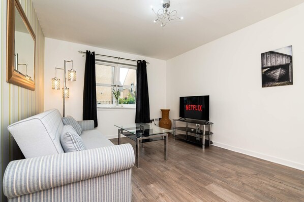 A modern living room with a sofa, a glass coffee table, a TV, and a painting on the wall.