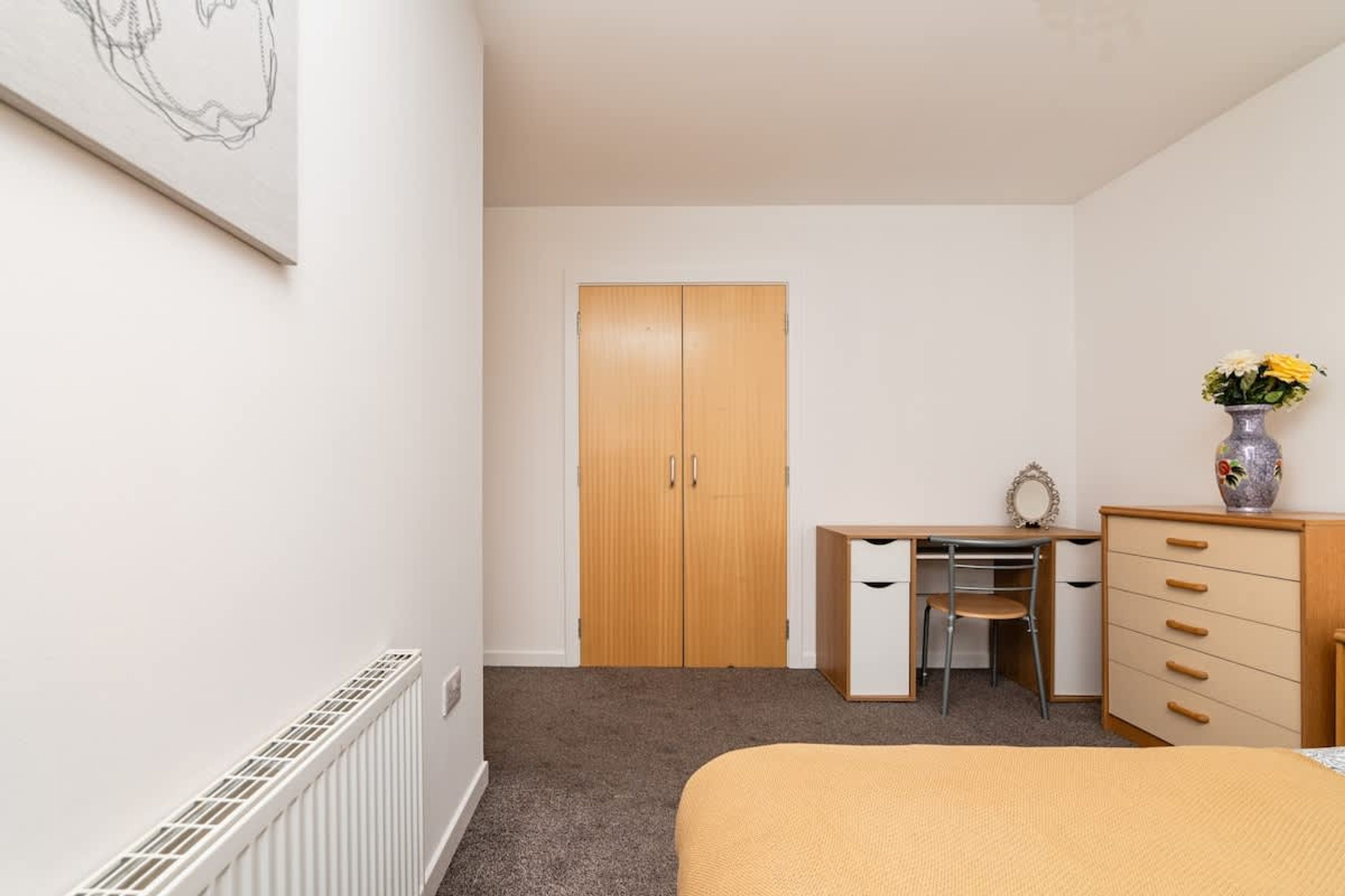 A bedroom with a bed, a desk with a chair, a wardrobe, and a radiator.