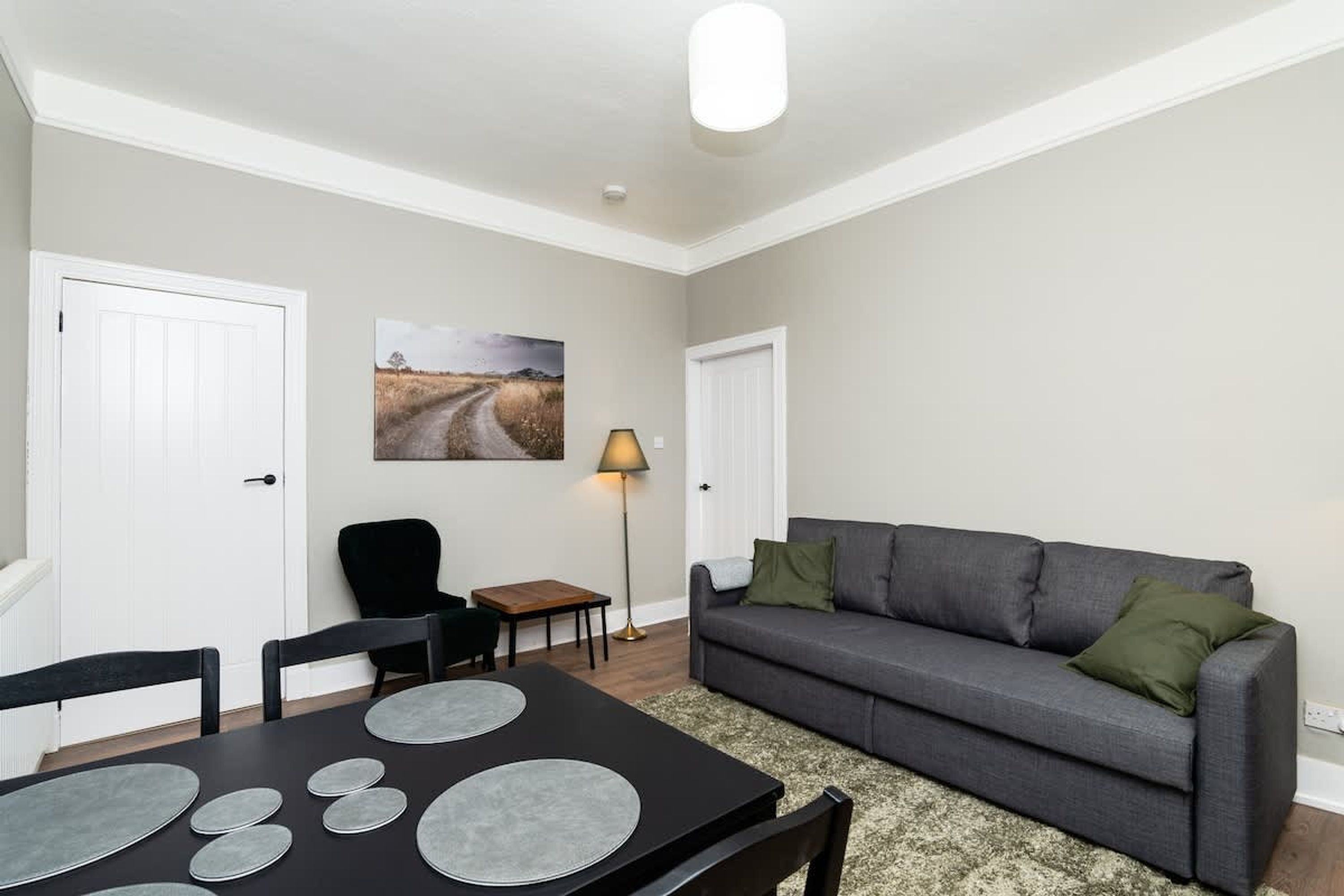 Un salon avec un canapé, une table à manger entourée de chaises, une lampe et un tableau accroché au mur.