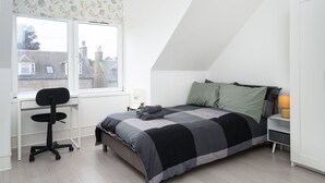 A bedroom with a bed, desk, chair, and a window with a view of houses. - Cosy Fully Equipped Studio 5 Close to University (Aberdeen)