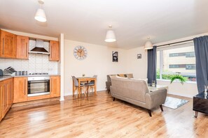 Un appartement moderne doté de meubles de rangement en bois, d’une table à manger, d’un canapé et d’une grande fenêtre agrémentée de rideaux.