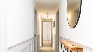 A narrow hallway with white walls, a wooden floor, and a mirror on the right. - 5 Bedroom Apartment - Galashiels (Galashiels)