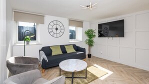 A modern living room with a sofa, armchairs, a round coffee table, and a large wall clock. - 5 Bedroom Apartment - Galashiels (Galashiels)