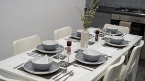 Una mesa de comedor dispuesta con platos, tazones, cubiertos, vasos y un florero con una planta.
