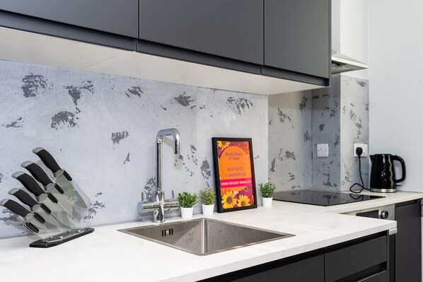 A modern kitchen with a granite countertop, a stainless steel sink, a knife block, a coffee maker, and a framed sign. - 1 Bedroom Apartment-free Parking (Edinburgh)