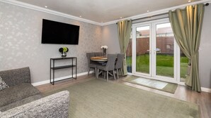 A living room with a flat-screen TV, a sofa, a dining table with chairs, and a sliding glass door leading to a backyard. - 3 Bedroom House-private Parking (Bonnyrigg)
