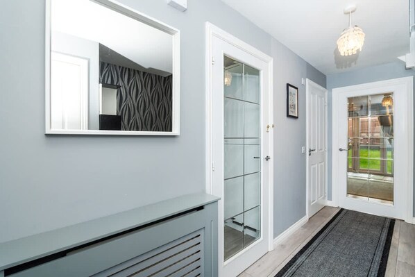 Un couloir avec un mur recouvert de miroirs, une porte en verre et un lustre.