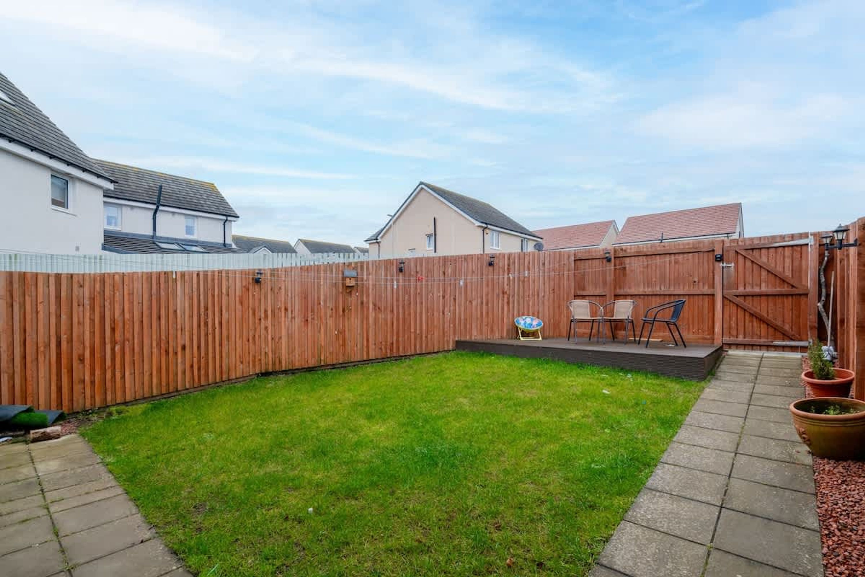 A backyard with a wooden fence, a grassy lawn, and a patio area with chairs and a table.