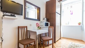 Een klein eetgedeelte met twee houten stoelen, een witte tafel, een televisie erboven en een magnetron op tafel.
