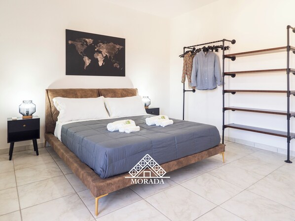 A neatly arranged bedroom with a bed, a world map on the wall, a clothing rack, and a logo. - Casa Maura - Morada - Three Bedroom Apartment, Sleeps 6 (Iglesias)