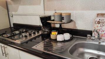 A kitchen with a gas stove, coffee maker, mugs, and a coffee-themed container.