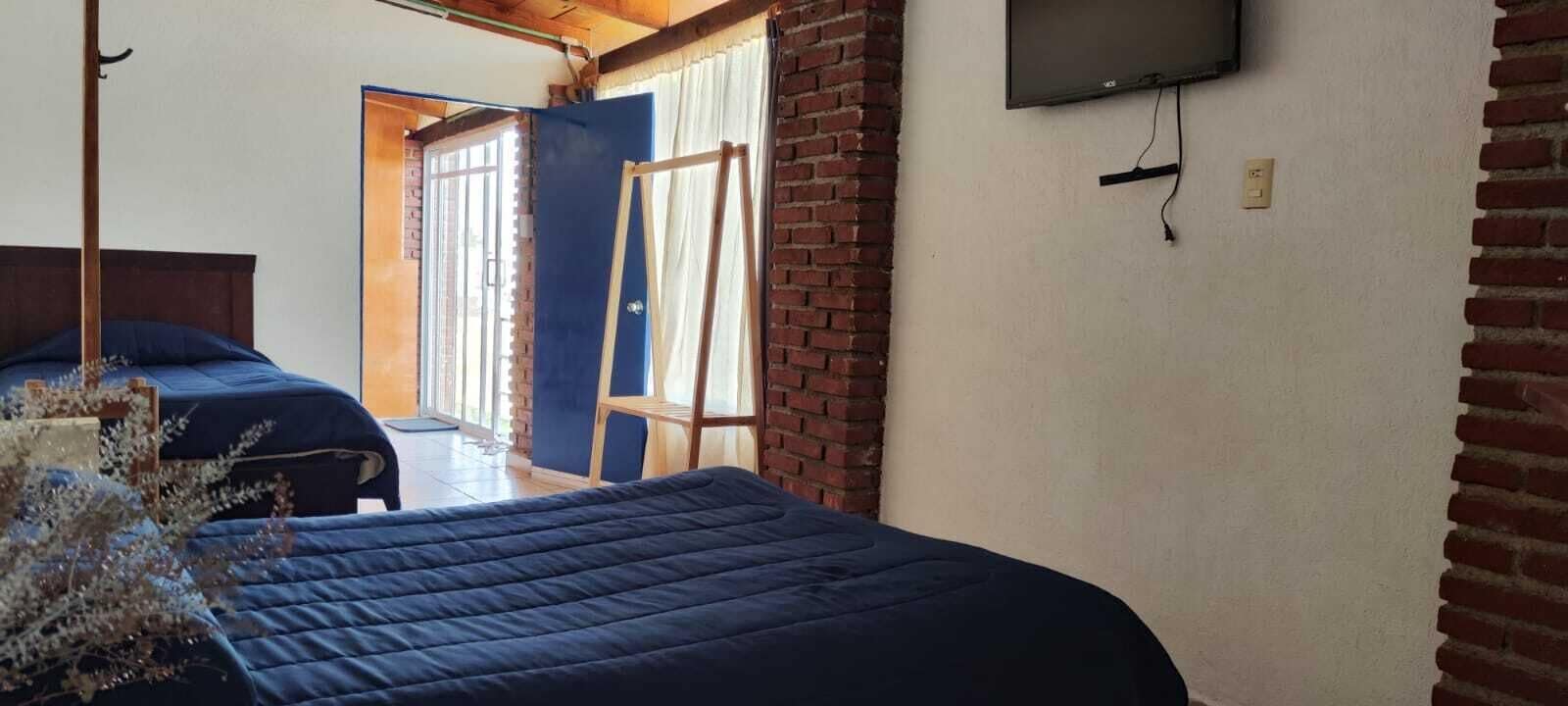 A room with two beds, a TV mounted on the wall, and a brick wall.