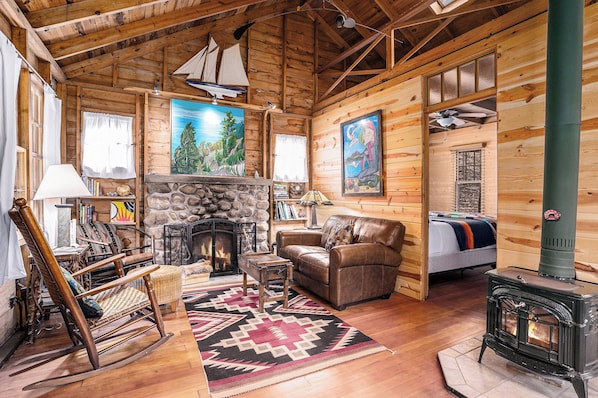 A cozy log cabin interior with a fireplace, a rocking chair, a leather sofa, and a bed.