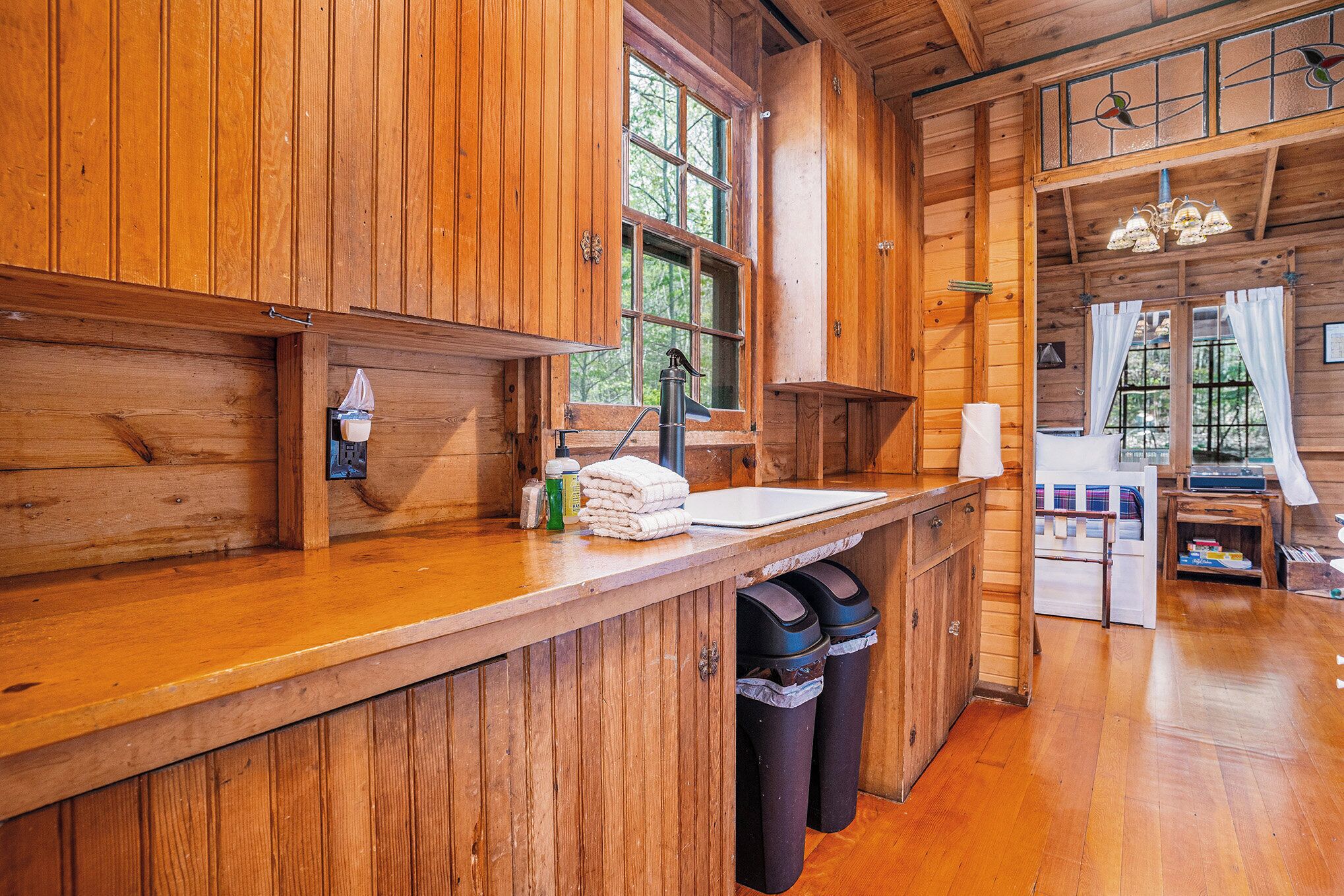 A wooden cabin kitchen with a wooden countertop, a sink, and two trash bins.