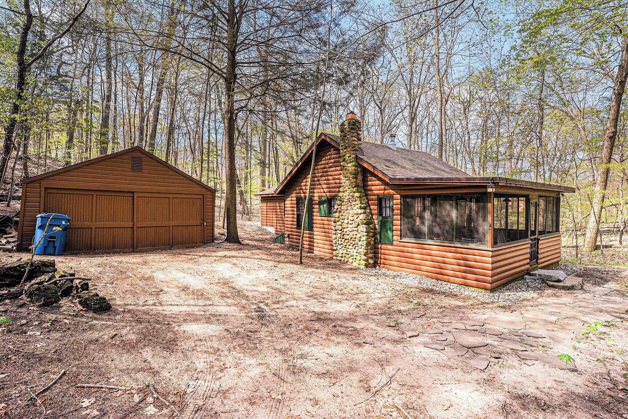Une cabane rustique avec une cheminée en pierre, un garage en bois et une véranda couverte.