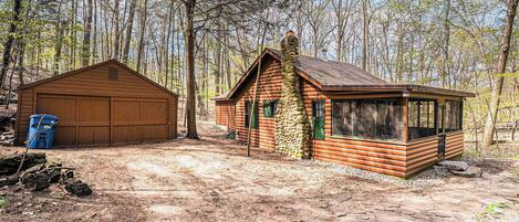 Une cabane rustique avec une cheminée en pierre, un garage en bois et une véranda couverte.