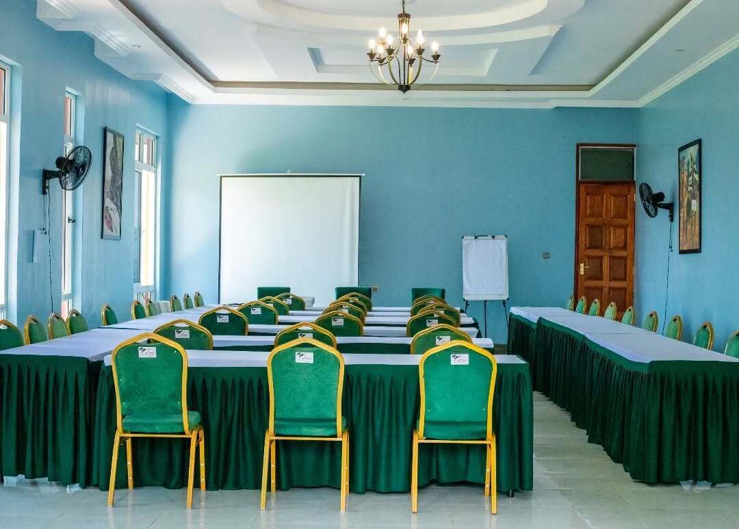 A conference room with green chairs and tables, a whiteboard, and a chandelier.